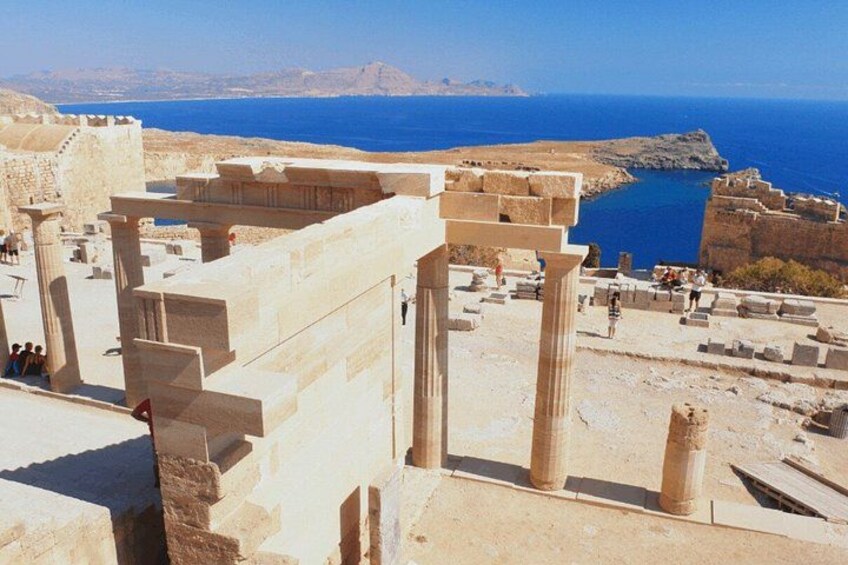 Ancient ruins with columns and steps, overlooking a body of water and distant mountains. 2