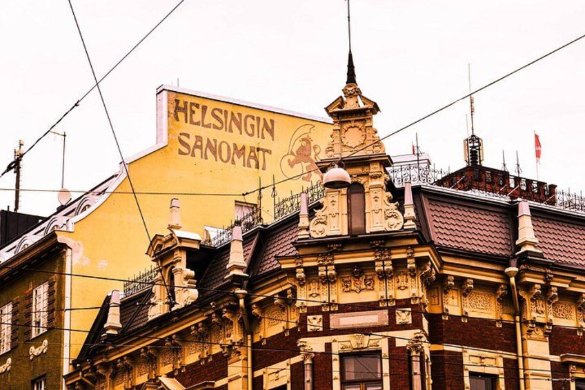 A building with ornate architectural details and a large sign reading 'HELSINGIN SANOMAT'. 5