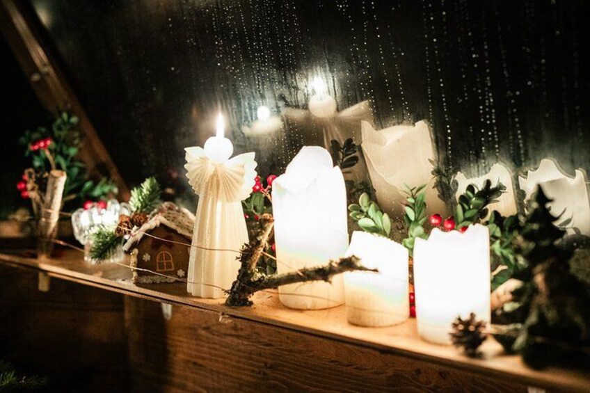 A wooden shelf with candles, a small house decoration, and greenery. 4