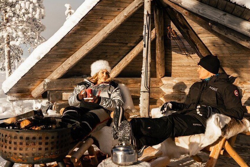 A person sitting on a wooden bench under a wooden roof, holding a cup, with a dog lying beside them. 4