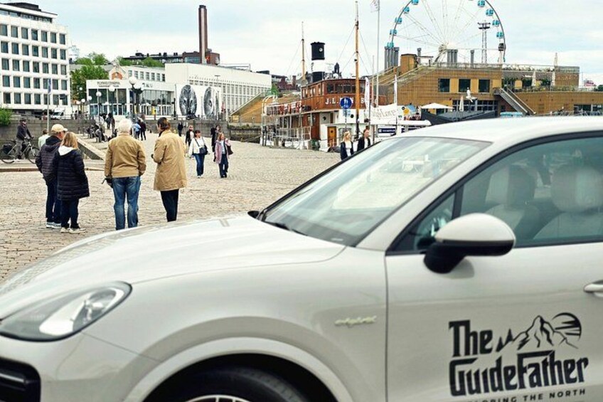 Ein weißes Auto mit dem Schriftzug 'The GuideFather' auf einer Kopfsteinpflasterstraße geparkt. 3