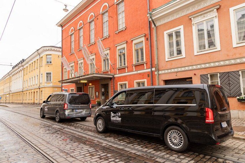 Ein schwarzer Kleinbus parkt auf einer Kopfsteinpflasterstraße, ein rotes Gebäude mit weißen Fenstern und ein gelbes Gebäude im Hintergrund. 4