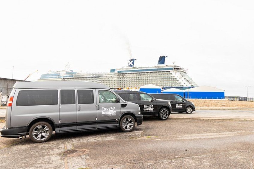 Una camioneta plateada y dos SUVs negros estacionados sobre una superficie de concreto, con un crucero al fondo. 1