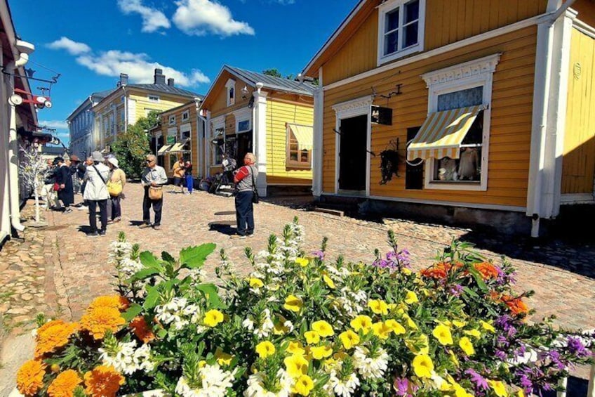 A cobblestone street with yellow buildings, people walking, and a flower bed in the foreground. 2