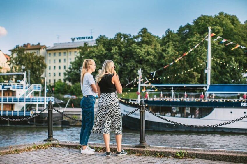 Two people standing by a waterfront with a boat and a building in the background. 4
