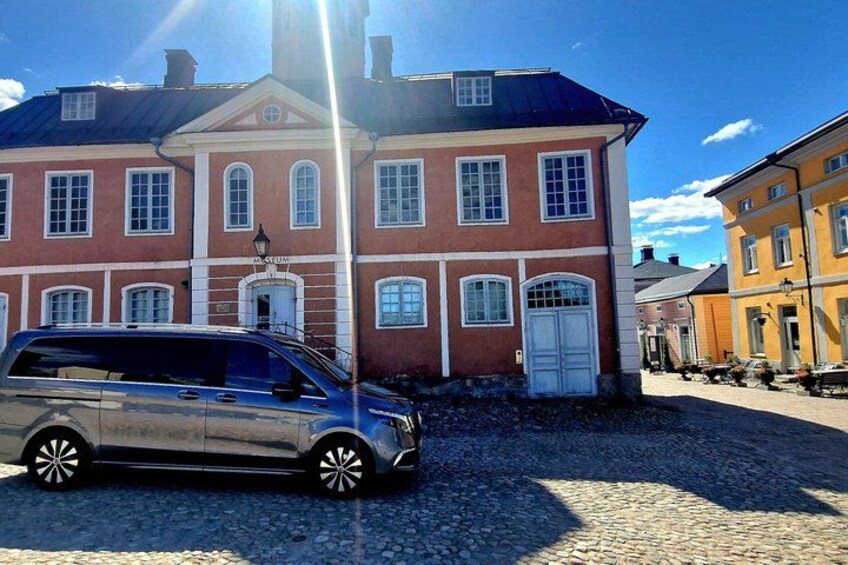 A red brick building with white trim, a parked car, and cobblestone pavement. 2