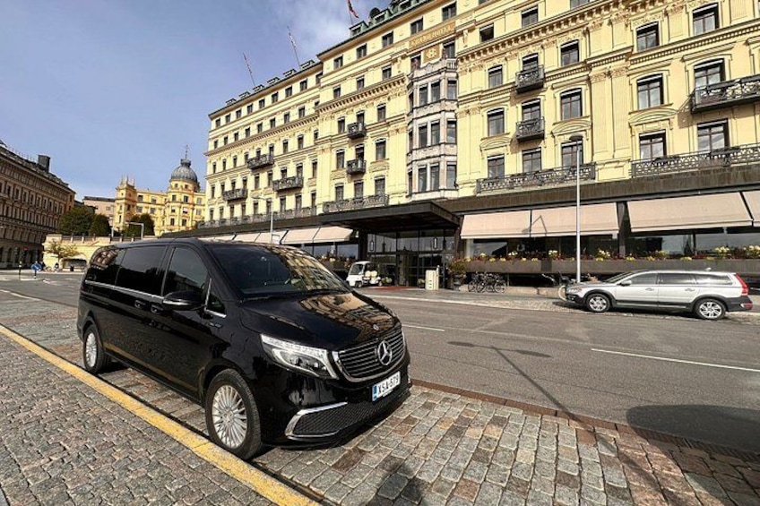 A black van parked on a cobblestone street, a yellow building with balconies, and a clear blue sky. 3