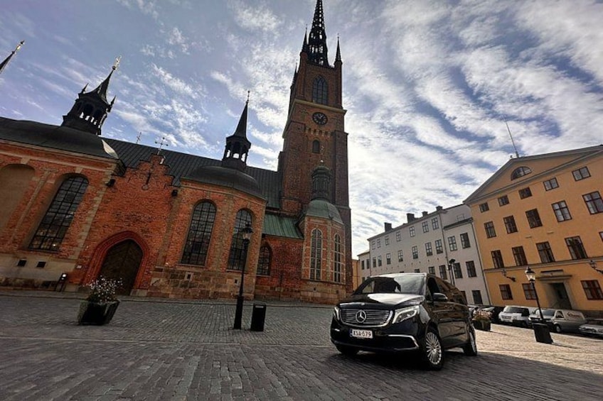 A historic building with a clock tower, a cobblestone plaza, and parked cars. 4