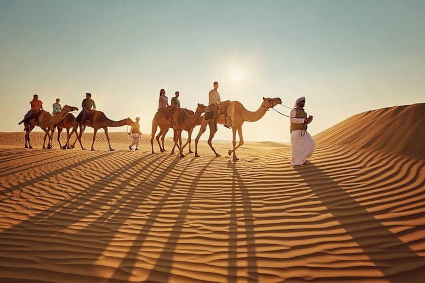 Un groupe de personnes chevauche des chameaux à travers un paysage désertique, avec des dunes de sable. 1