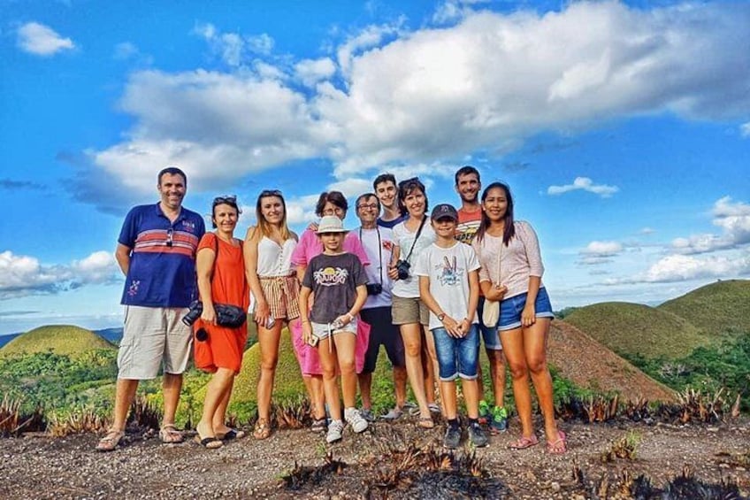 Un grupo de personas de pie sobre un sendero de tierra, con colinas verdes al fondo. 5