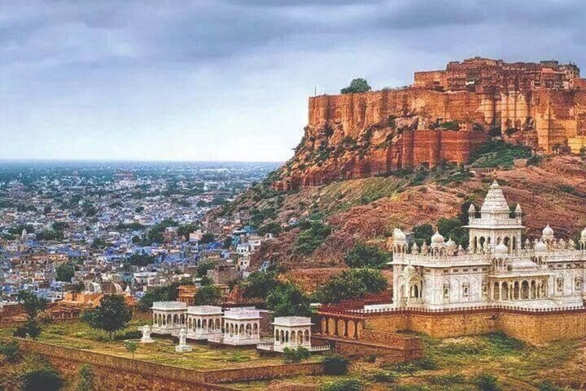 A historic fort on a hill overlooking a city, with a palace in the foreground. 2