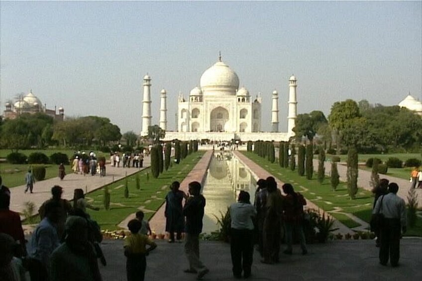 The Taj Mahal with a reflection in the water, surrounded by a garden and visitors. 3