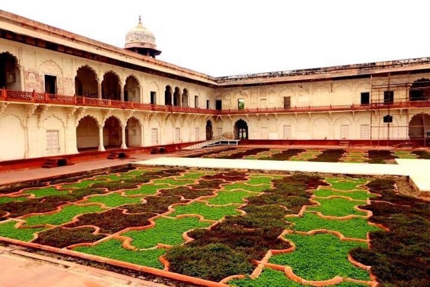 A courtyard with patterned gardens and a building with arches. 2