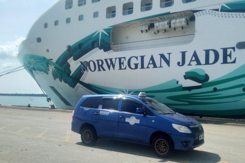 Un'auto blu parcheggiata di fronte a una grande nave, la Norwegian Jade, con decorazioni verde e bianco. 1