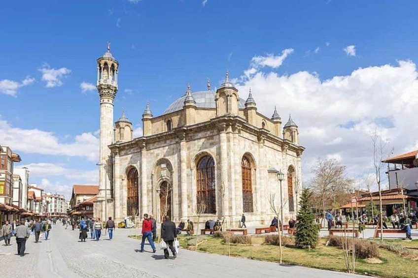 A historic building with arched windows and a minaret, surrounded by a plaza with people walking. 4