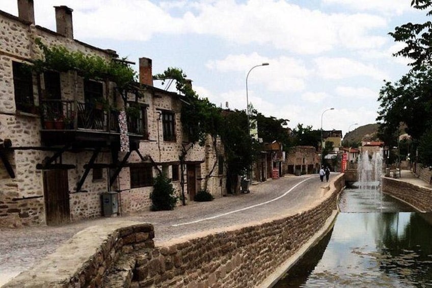 A narrow street with stone buildings, a canal, and a fountain. 3