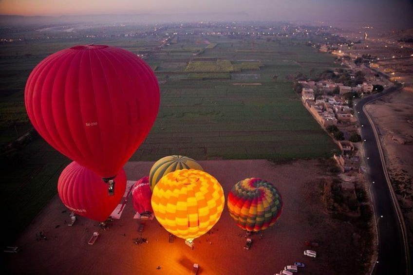 A group of hot air balloons over a rural landscape with fields and a road. 3