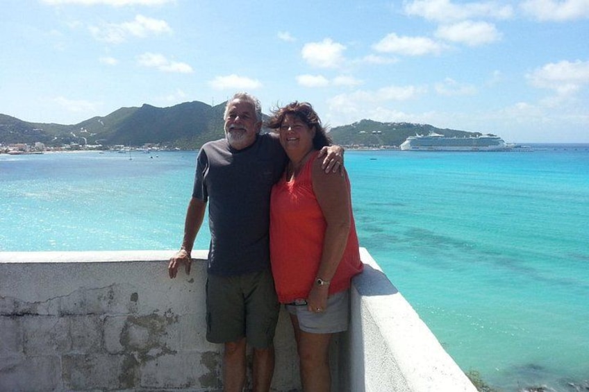Two people standing by a waterfront with a cruise ship in the background. 2