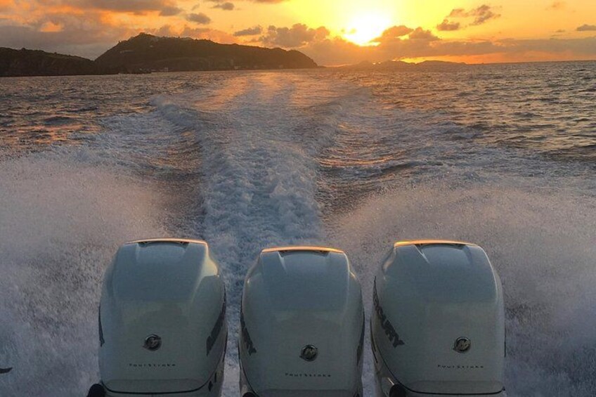 A boat with three outboard motors on a body of water during sunset. 1