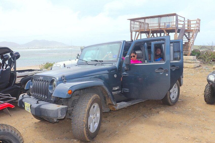A blue off-road vehicle parked on a dirt area with a wooden structure in the background. 1