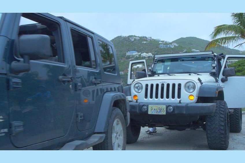 Two off-road vehicles parked on a road with a mountainous landscape in the background. 2