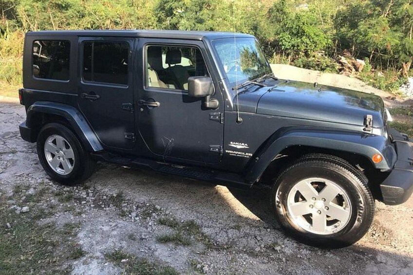A black off-road vehicle parked on a gravel path with greenery in the background. 1