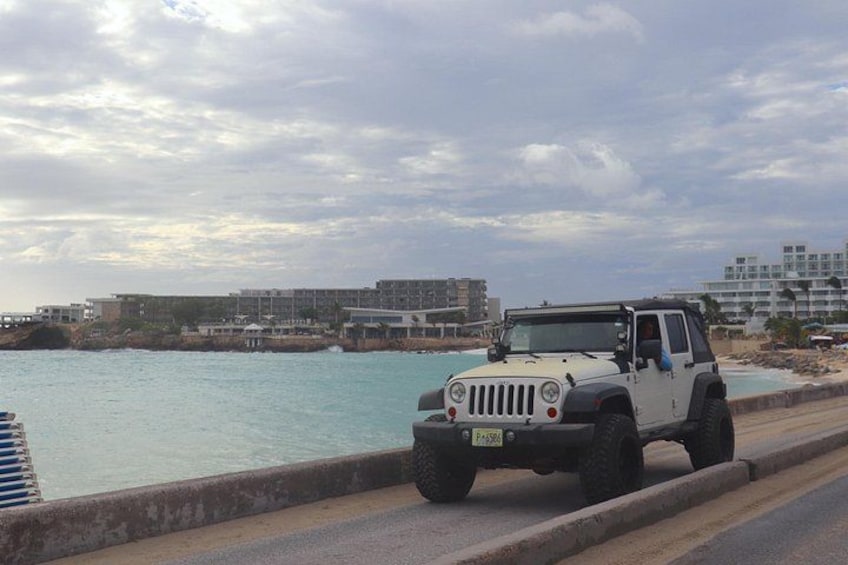 A white off-road vehicle parked by a waterfront with buildings in the background. 3
