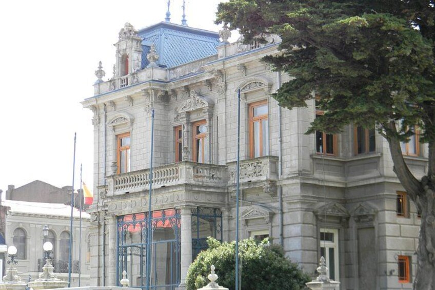 Un edificio histórico con arquitectura ornamentada, una fuente en primer plano y una bandera al fondo. 2