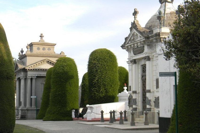 A cemetery with neatly trimmed hedges, a white monument, and classical architecture. 1