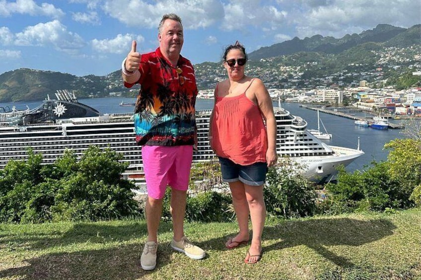 Dos personas de pie sobre césped, con un crucero y un puerto al fondo. 4
