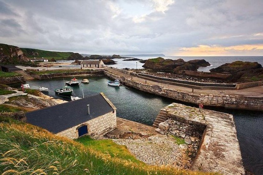 A coastal harbor with boats, a stone wall, and a grassy hill. 3