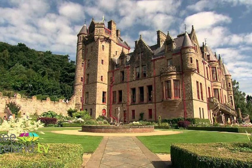A large, historic castle with multiple towers and turrets, surrounded by well-manicured gardens and a clear sky. 5