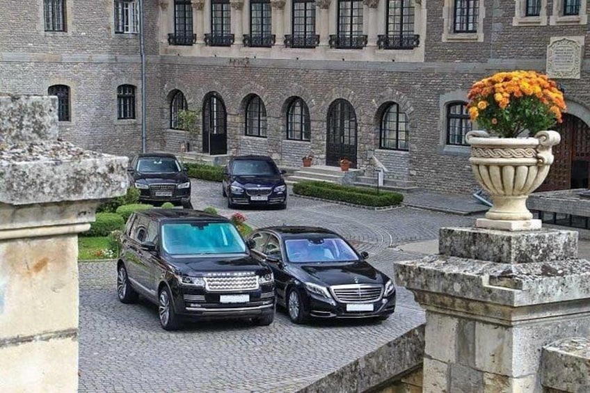 A courtyard with parked cars, a stone building, and a large flower pot. 4