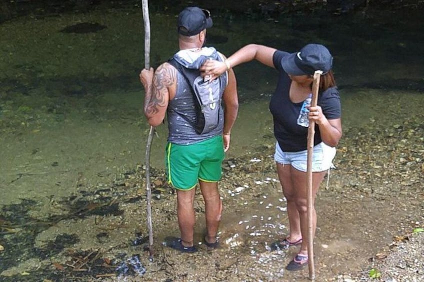 Two people standing by a river, one holding a walking stick. 4