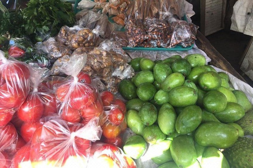 A market stall with bags of red apples, green avocados, and other produce. 1