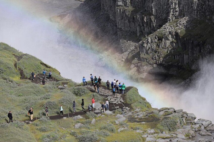 Un grupo de personas en un saliente rocoso con vistas a una cascada y un arcoíris. 5