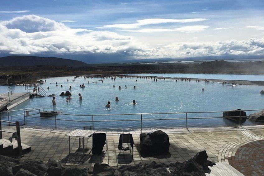Un spa geotérmico con varias fuentes termales, una terraza de madera y un telón de fondo montañoso. 3