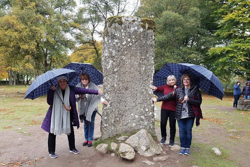 Four people standing near a stone monument in a park with autumn trees in the background. 1