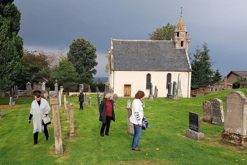 A cemetery with gravestones, a church, and people walking. 4