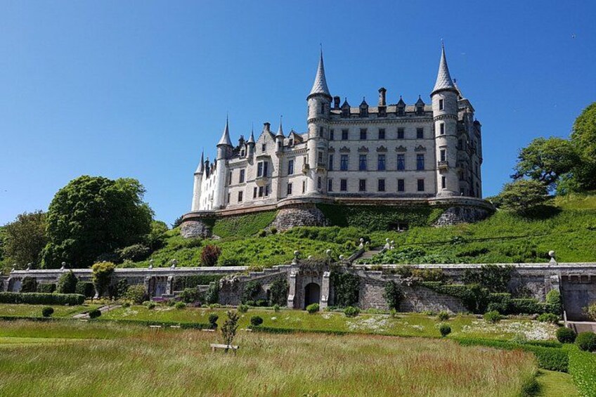 Een kasteel met meerdere torens, omgeven door weelderige groene begroeiing en een verzorgde tuin. 4