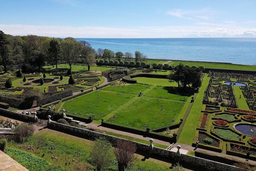 Een aangelegde tuin met geometrische patronen, een groot centraal gazon en een waterpartij op de achtergrond. 2