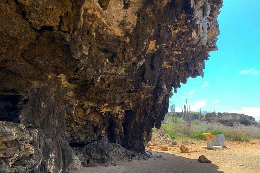 A large rock formation with a cave entrance, desert landscape, and sparse vegetation. 1