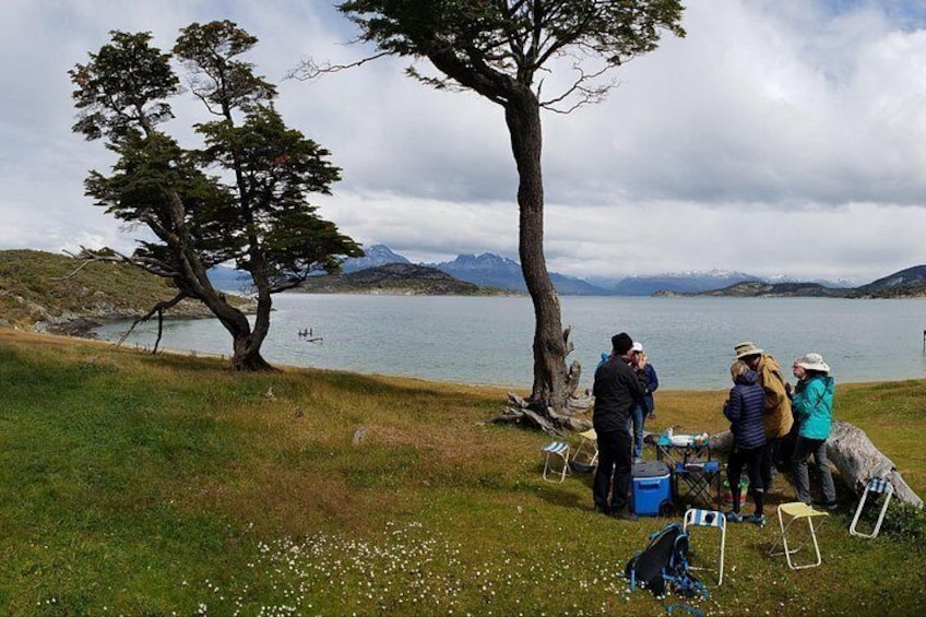 A group of people gathered around a table near a lake with mountains in the background. 3