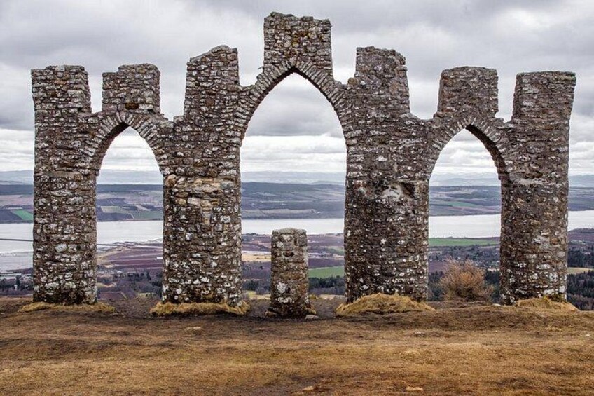 A ruined stone structure with arches, surrounded by a hilly landscape and a body of water in the distance. 3
