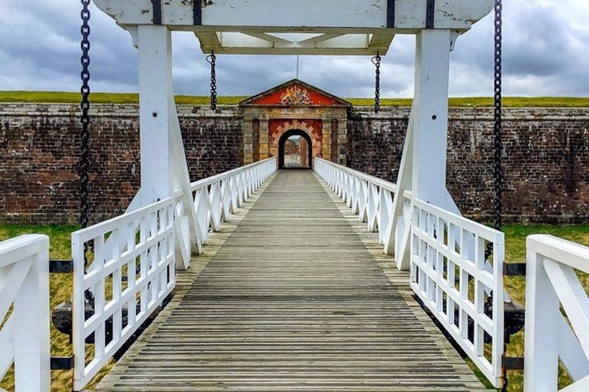 A wooden bridge with white railings leading to a brick structure with a red roof. 4