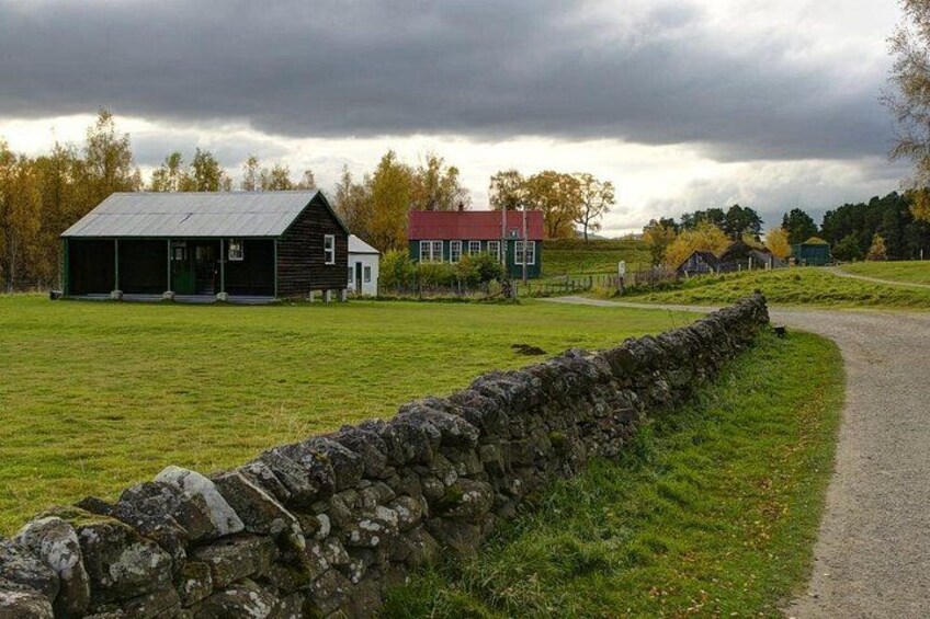 Een landelijk landschap met een stenen muur, een zwart schuurtje en een huis met een rode dak. 4