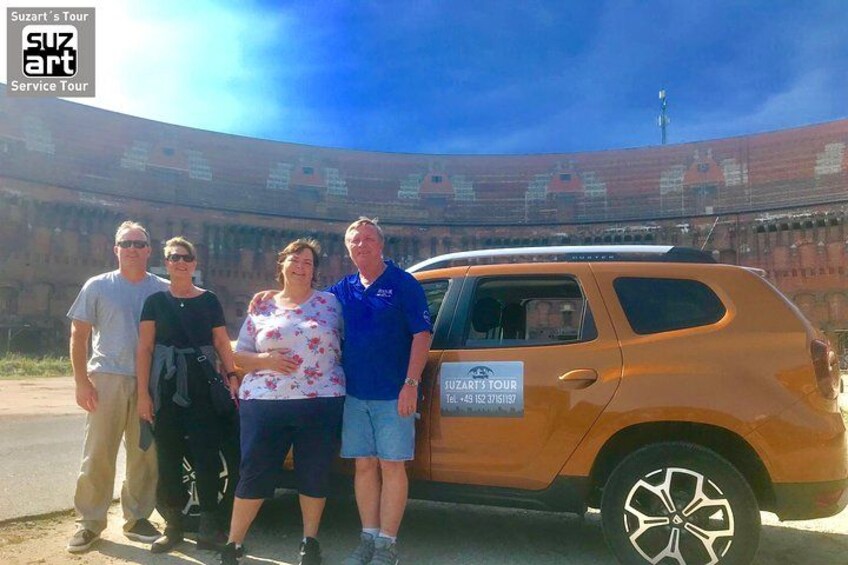 Un grupo de personas de pie frente a un estadio grande con un vehículo de recorrido turístico. 4