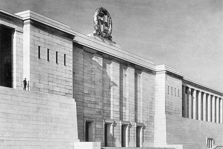 Un edificio amplio y moderno con una entrada destacada y un emblema decorativo sobre las puertas. 2