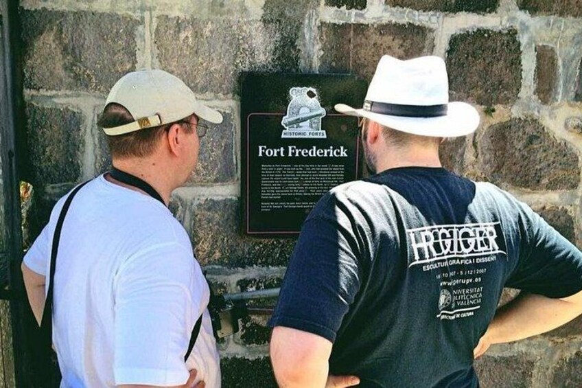 Two men standing in front of a stone wall with a plaque that reads 'Fort Frederick.' 1