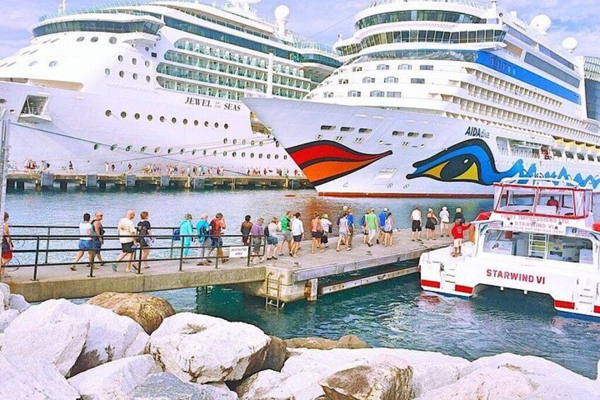 A cruise ship docked at a port with a pier, people walking on the pier, and another ship named 'STARWIND VI' in the foreground. 2